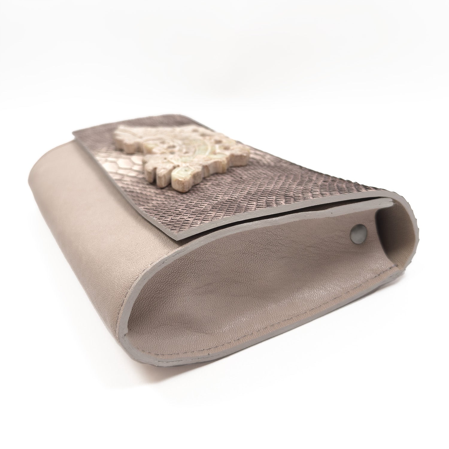 A pink nude leather clutch from evokewomen, featuring an embossed snake pattern and adorned with decorative stone embellishments.