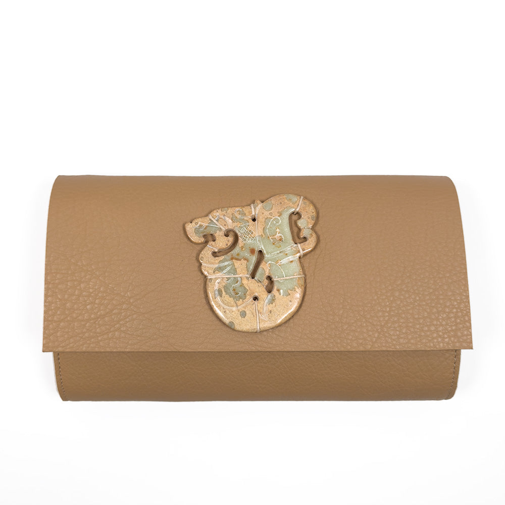 The BAGUETTE - CAMEL by evokewomen is a brown leather baguette clutch that showcases a decorative abstract emblem on the front, expertly crafted from exquisite Italian leather.