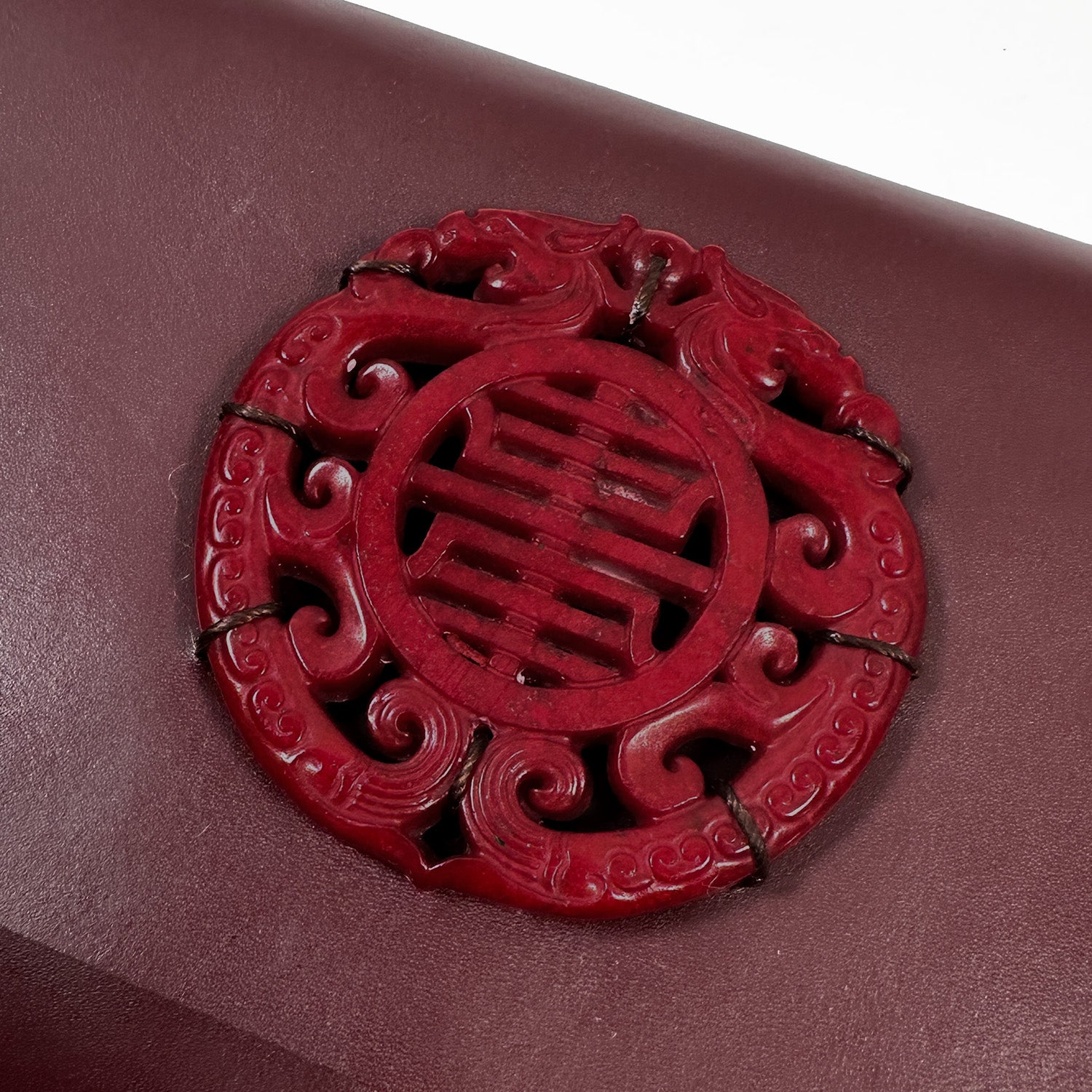 A BAGUETTE - BURGUNDY by evokewomen features a carved red circular emblem with intricate patterns, evoking the elegance of Italian leather craftsmanship.