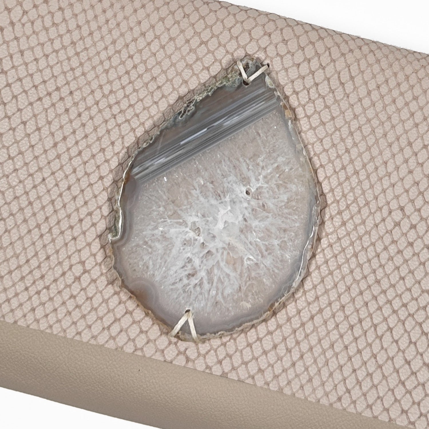 Detail of teardrop-shaped white crystal and grey agate on powder hued snake embossed leather.