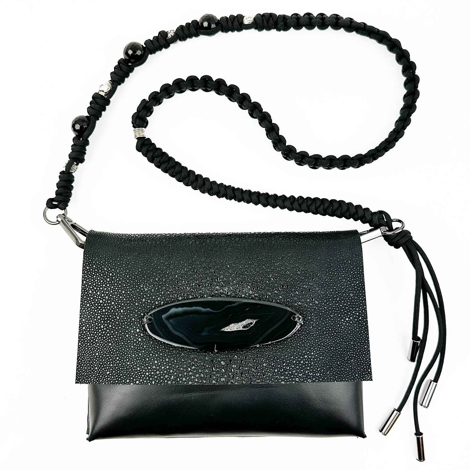 Introducing the BAHAMA - BLACK STINGRAY - KNOTTED STRAP by evokewomen, featuring a clutch crafted from Italian leather with a textured flap, decorative oval detail, and a braided strap adorned with bead accents.