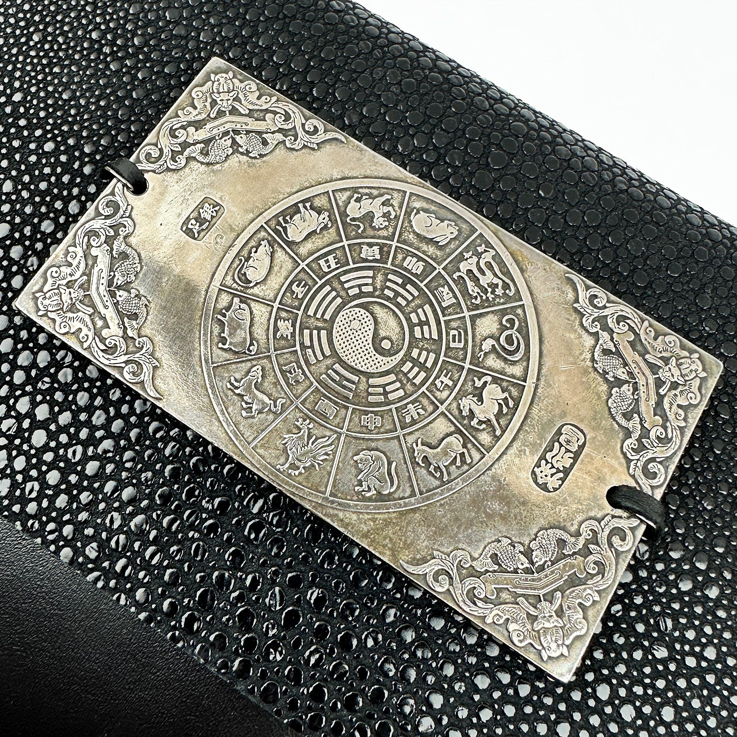 A rectangular metal plaque showcasing the Chinese zodiac animals, a yin-yang symbol, and intricate designs on a textured black surface, exudes the elegance akin to evokewomen's BAHAMA - BLACK STINGRAY.