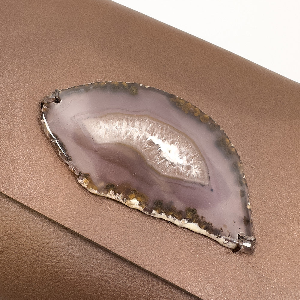 The BAHAMA - nutshell bag by evokewomen features a polished agate slice with a white crystalline center, beautifully attached to its brown Italian leather surface, enhancing its sophisticated design.
