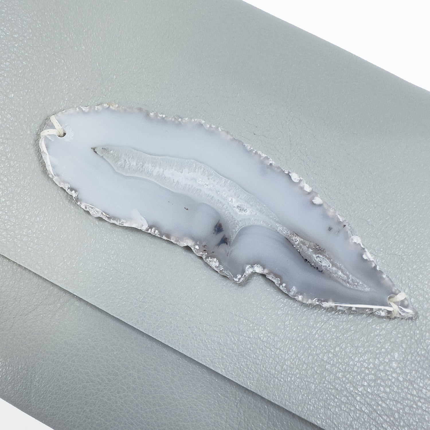 A light smoke-toned Bahama bag from evokewomen, featuring a knotted strap, displays a gray agate slice with a wavy pattern on its luxurious Italian leather, enhancing its elegance.
