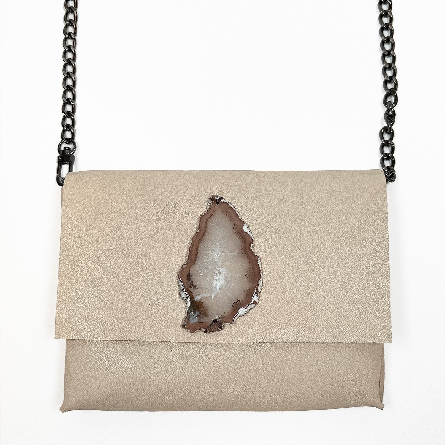 The BAHAMA - almond bag by evokewomen showcases luxurious Italian leather in a soft beige tone, paired with an elegantly knotted strap. Its unique charm is heightened by the signature agate slice embedded in the flap, making this sophisticated accessory truly stand out.
