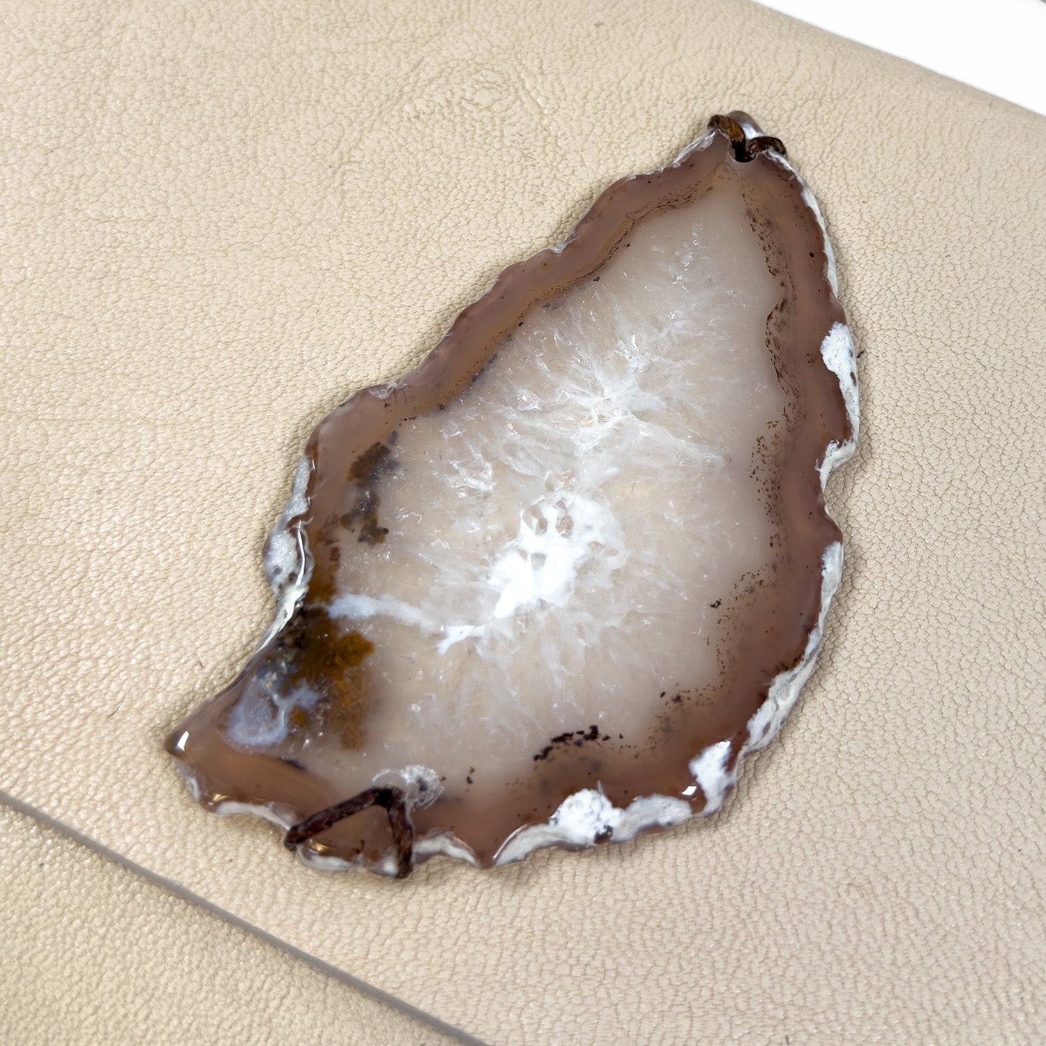 The BAHAMA - almond - knotted strap by evokewomen rests elegantly on a beige textured surface, echoing the refined aesthetic of Italian leather.
