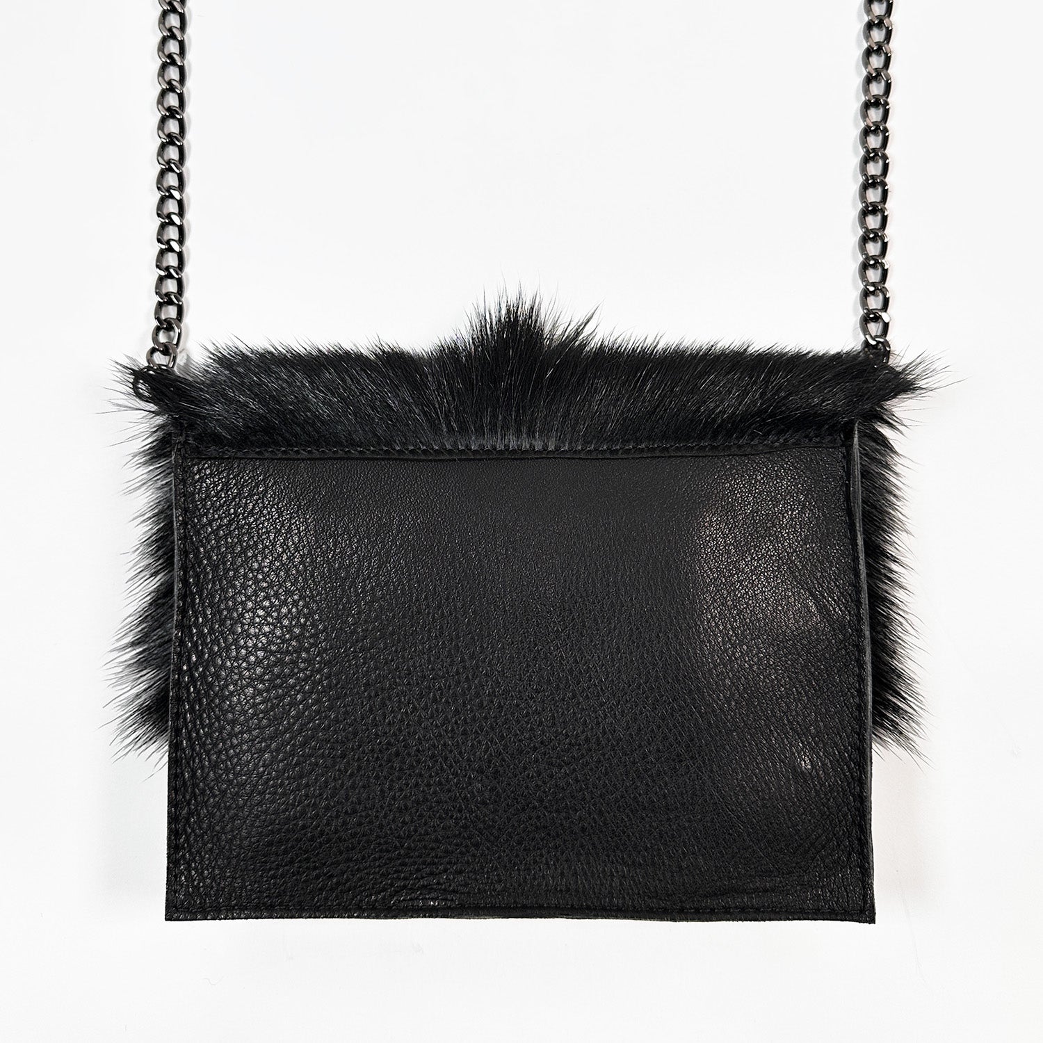The BAHAMA FUR - BLACK by evokewomen is a luxurious textured leather bag in black, adorned with a chain strap and sophisticated fur trim, beautifully showcased against a pristine white background.