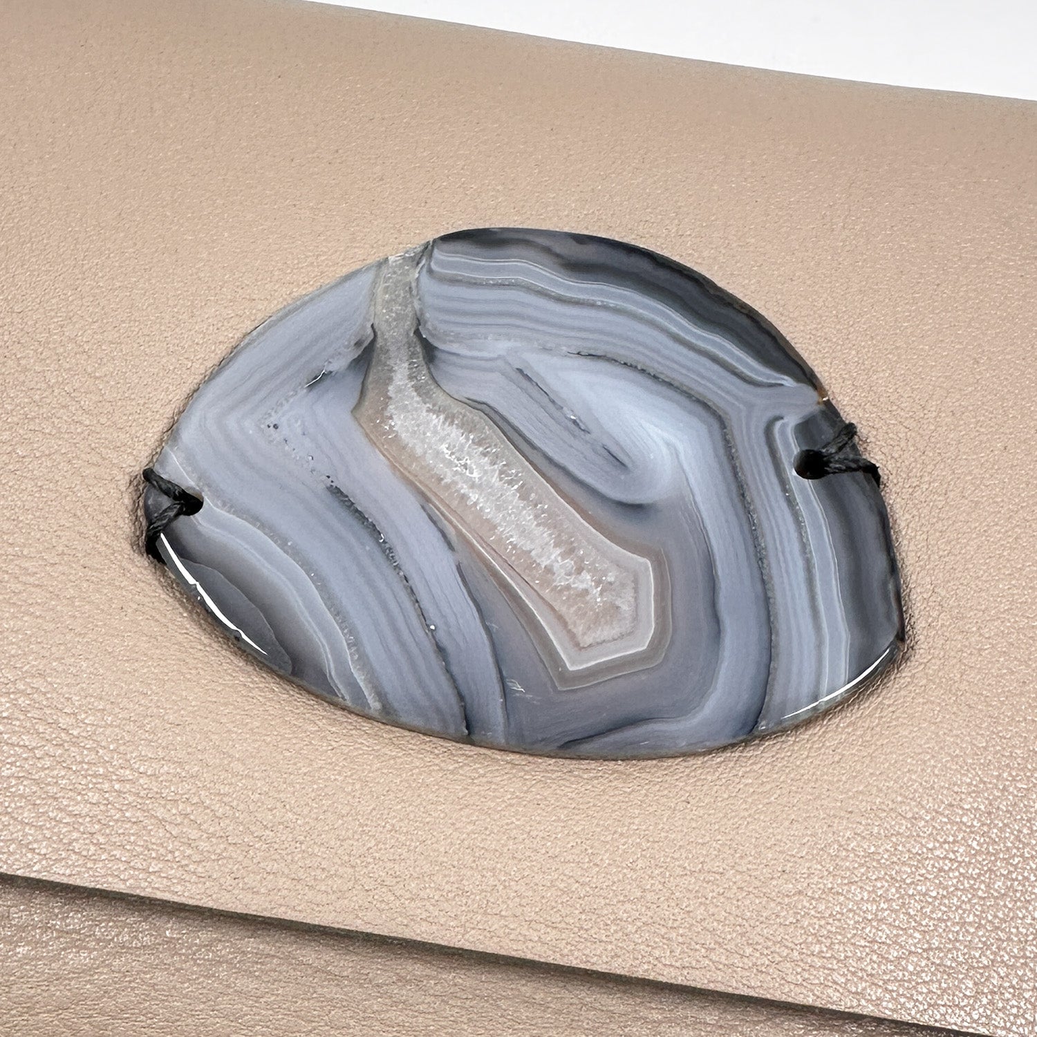 Close-up of a gray and white banded agate stone with natural crystal formations, set into taupe pebbled leather.