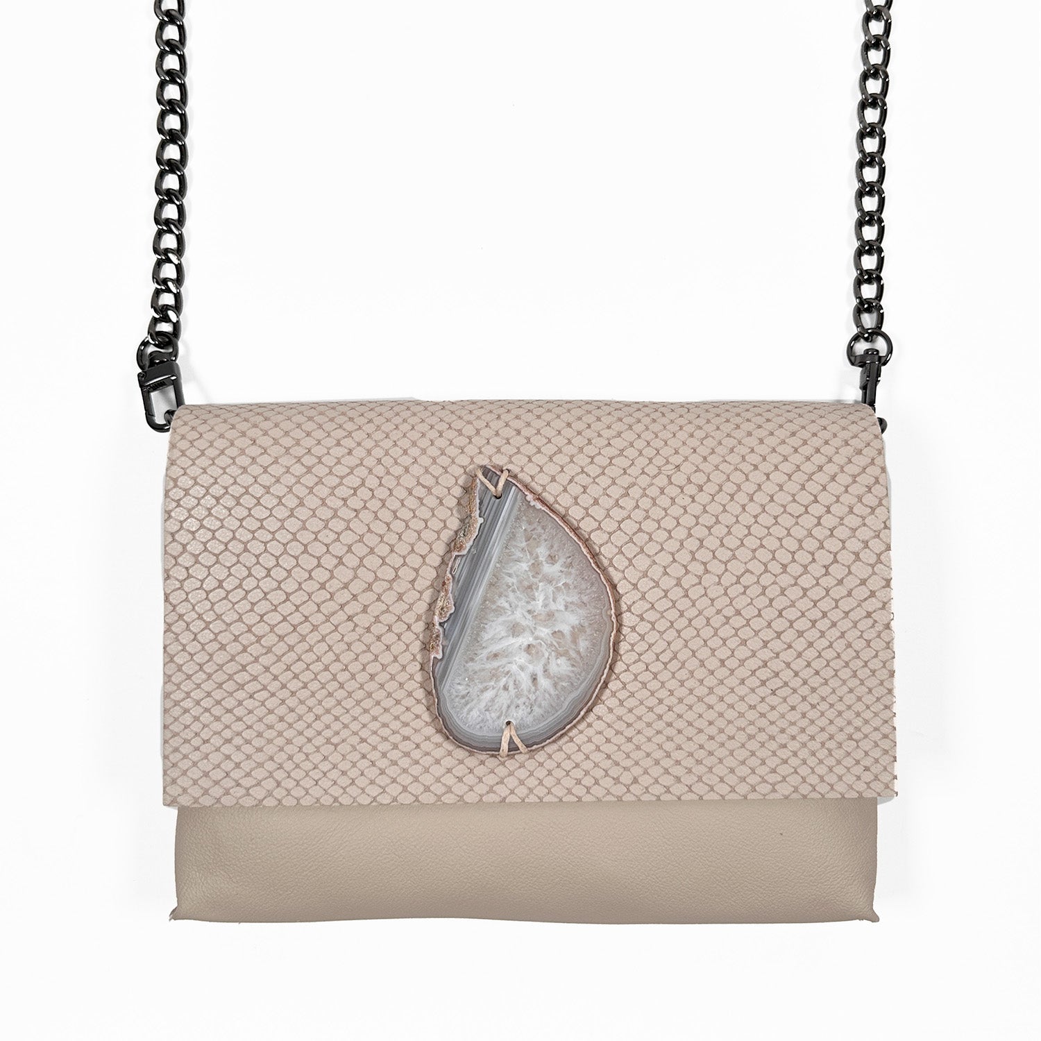 Powder hued leather crossbody bag featuring a textured, snakeskin-embossed flap and a teardrop-shaped white druzy agate stone centerpiece, paired with a black gunmetal chain strap.