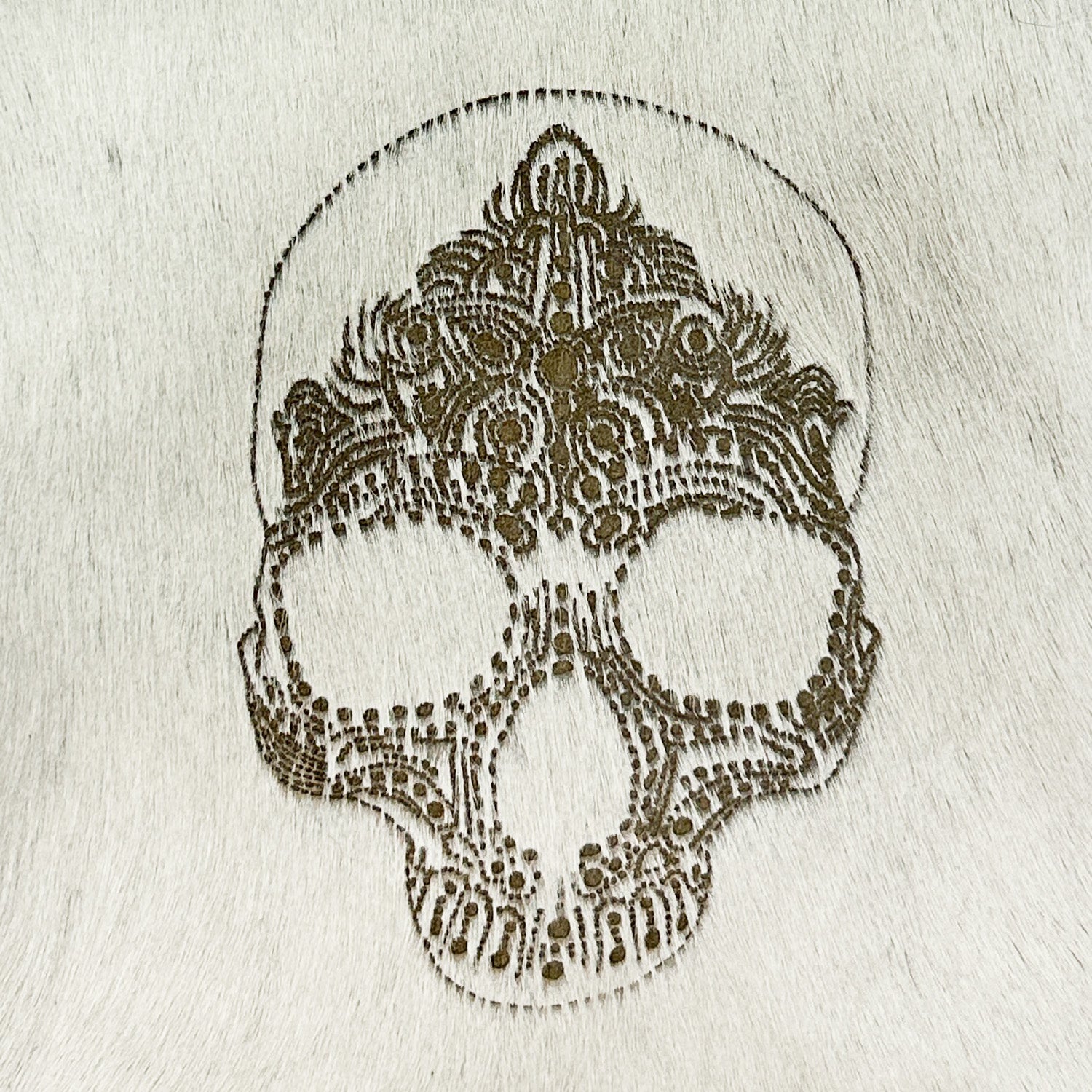 The ENYA - OFF-WHITE LASER SKULL by evokewomen showcases an elaborate laser-etched decorative skull pattern on a textured Italian leather surface, highlighting intricate and symmetrical details.