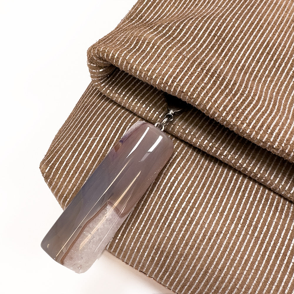 The versatile accessory crafted by evokewomen, known as the Farah - nutshell-silver, showcases a chic design with brown quilted fabric adorned with white stripes and features a rectangular, semi-transparent pendant attached to a zipper, effortlessly combining style and function.