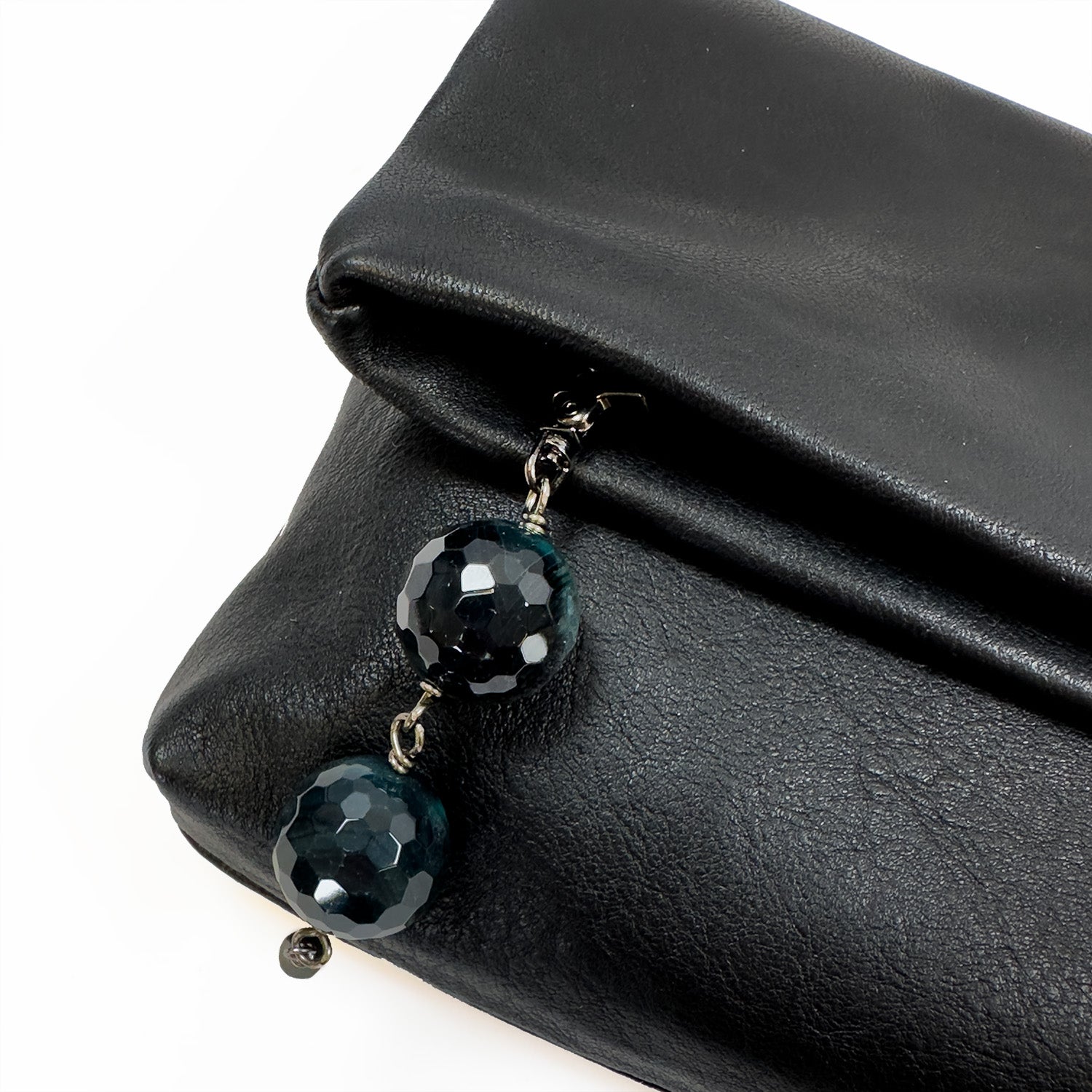 The versatile Farah clutch in black leather by evokewomen features a sleek zipper adorned with two large faceted black beads, complemented by a stylish snake spine chain.