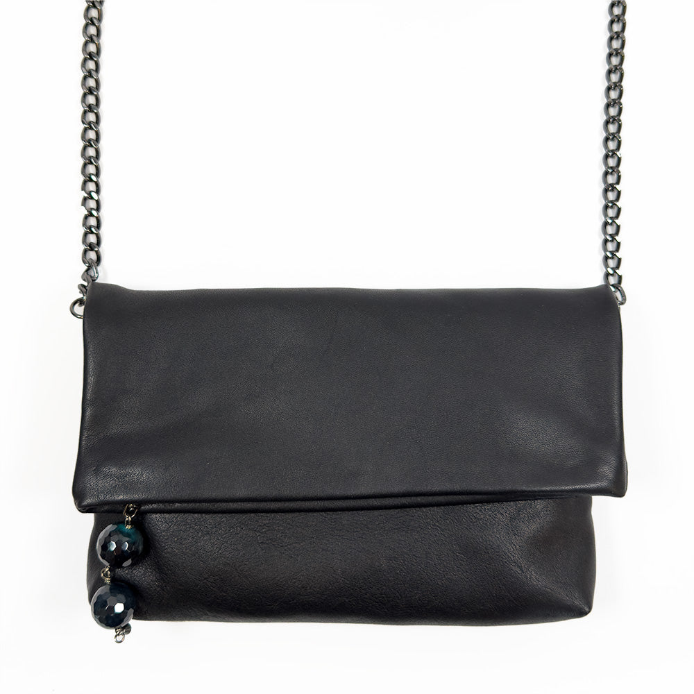 The versatile Farah - black by evokewomen is a chic fold-over clutch crafted from black leather, featuring a stylish snake spine chain strap and adorned with two decorative beads on the side.