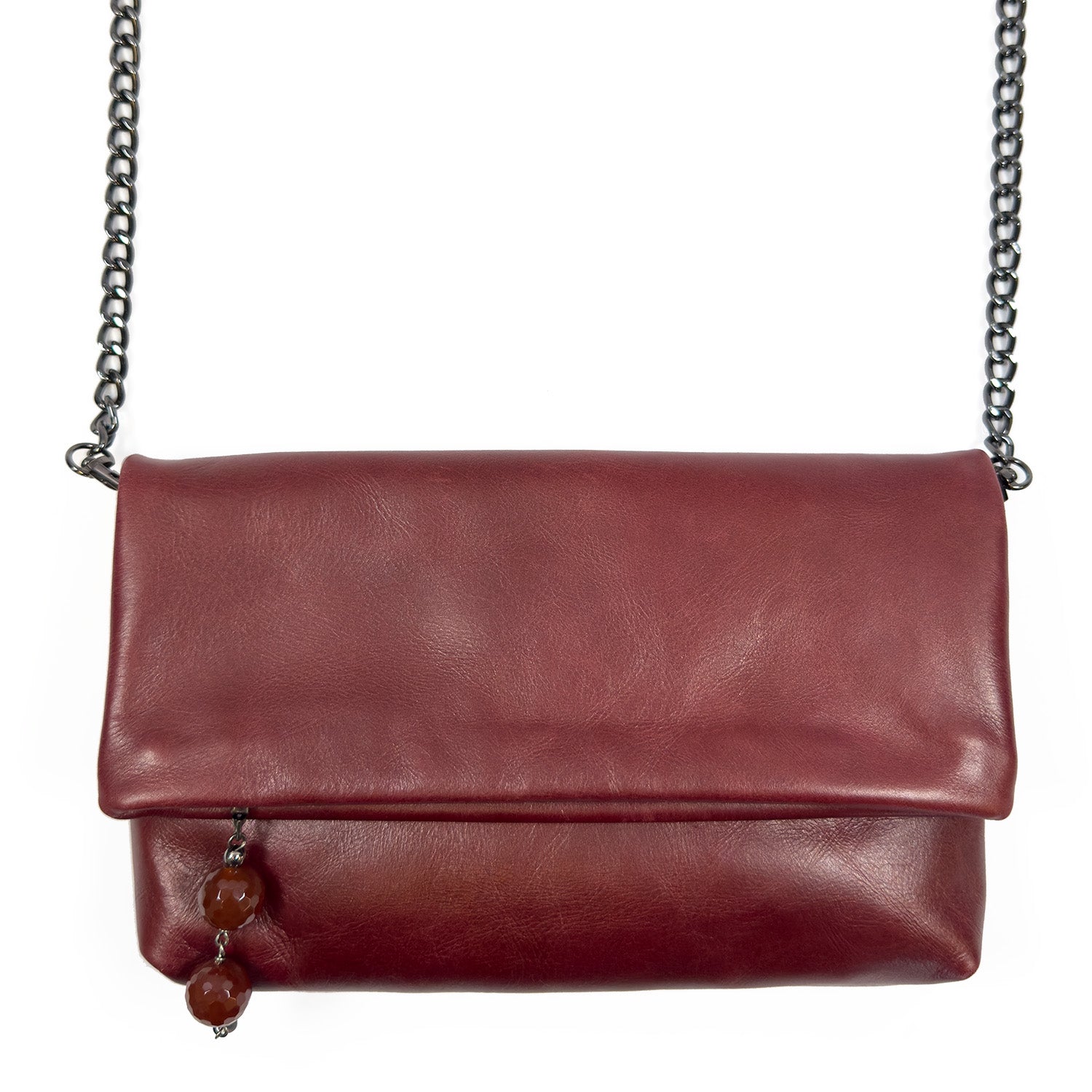 The "Farah - wine" by evokewomen is a cross-body bag made of maroon leather, featuring a chain strap and two decorative beads on one side, combining elegance with practicality.