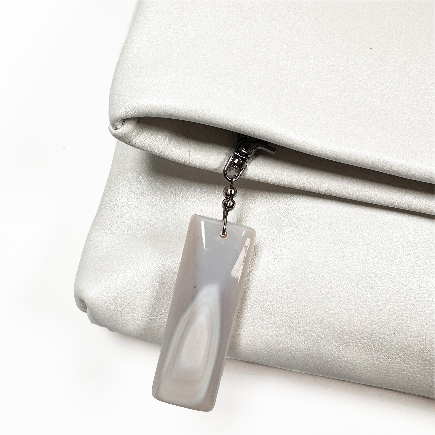 Introducing the Farah - pearl white by evokewomen: a versatile clutch crafted from high-quality leather, featuring a striking stone zipper charm that adds elegance to its design.