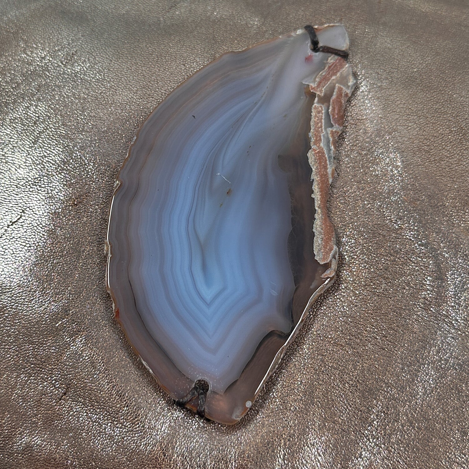 Detail of tear-drop shaped grey-blue and brown agate on metallic brown leather.