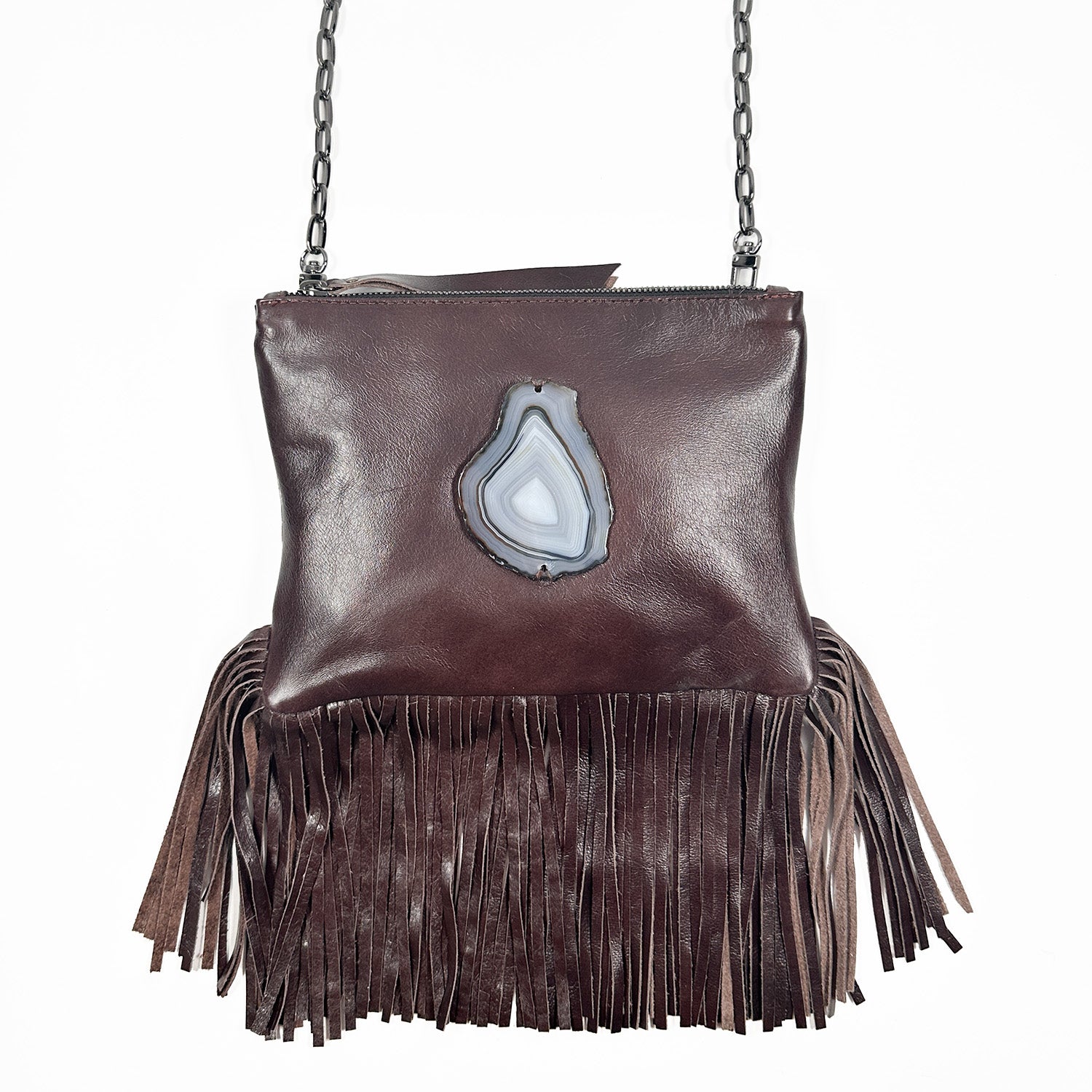 Reddish brown cross-body bag with zipper closure, fringes at bottom and teardrop shaped grey-black agate on white background. Gunmetal cross-body chain.
