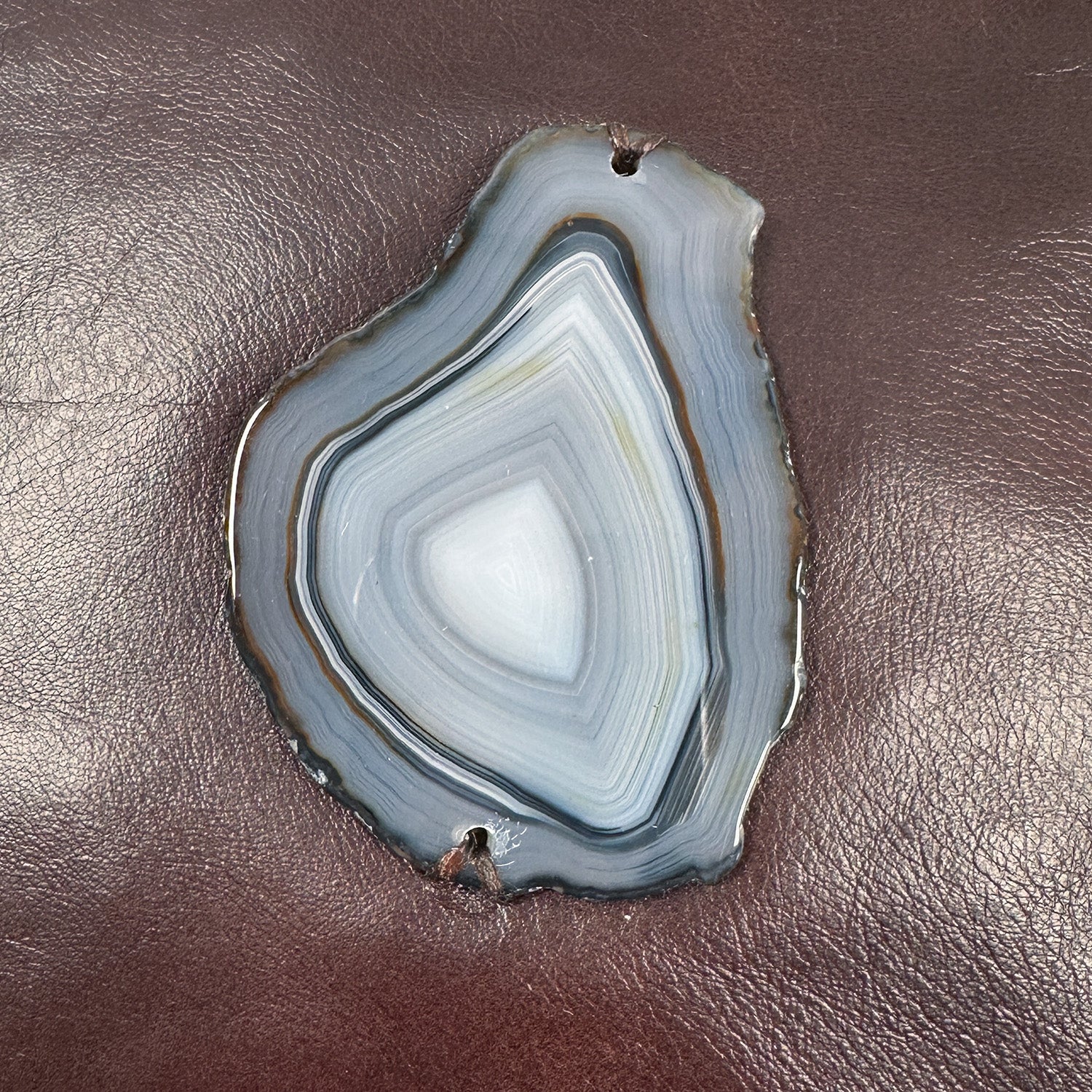 Detail of tear-drop shaped ringed grey, blue and brown agate on reddish brown leather.