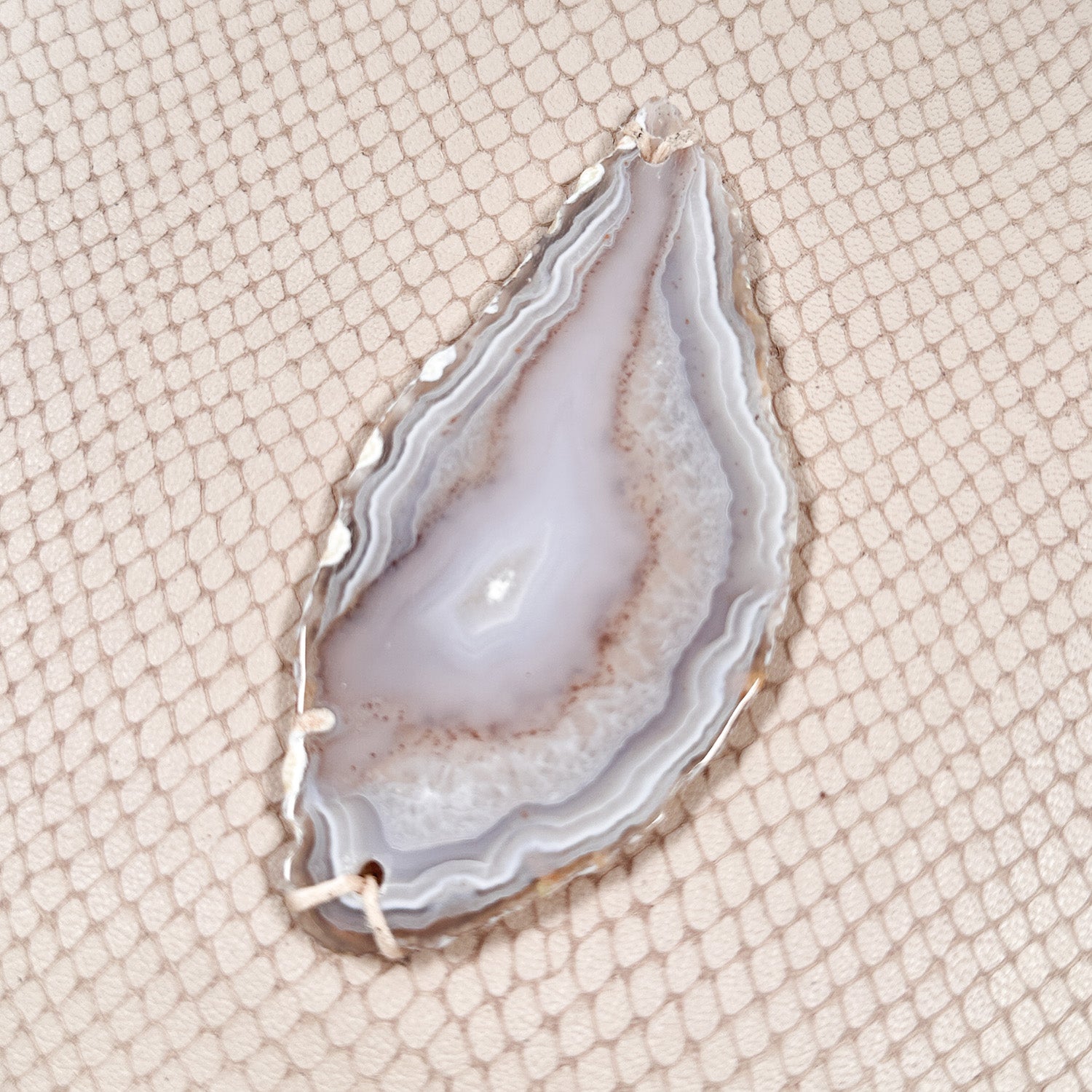 Detail of tear-drop shaped light colored agate on powder hued snake embossed leather.