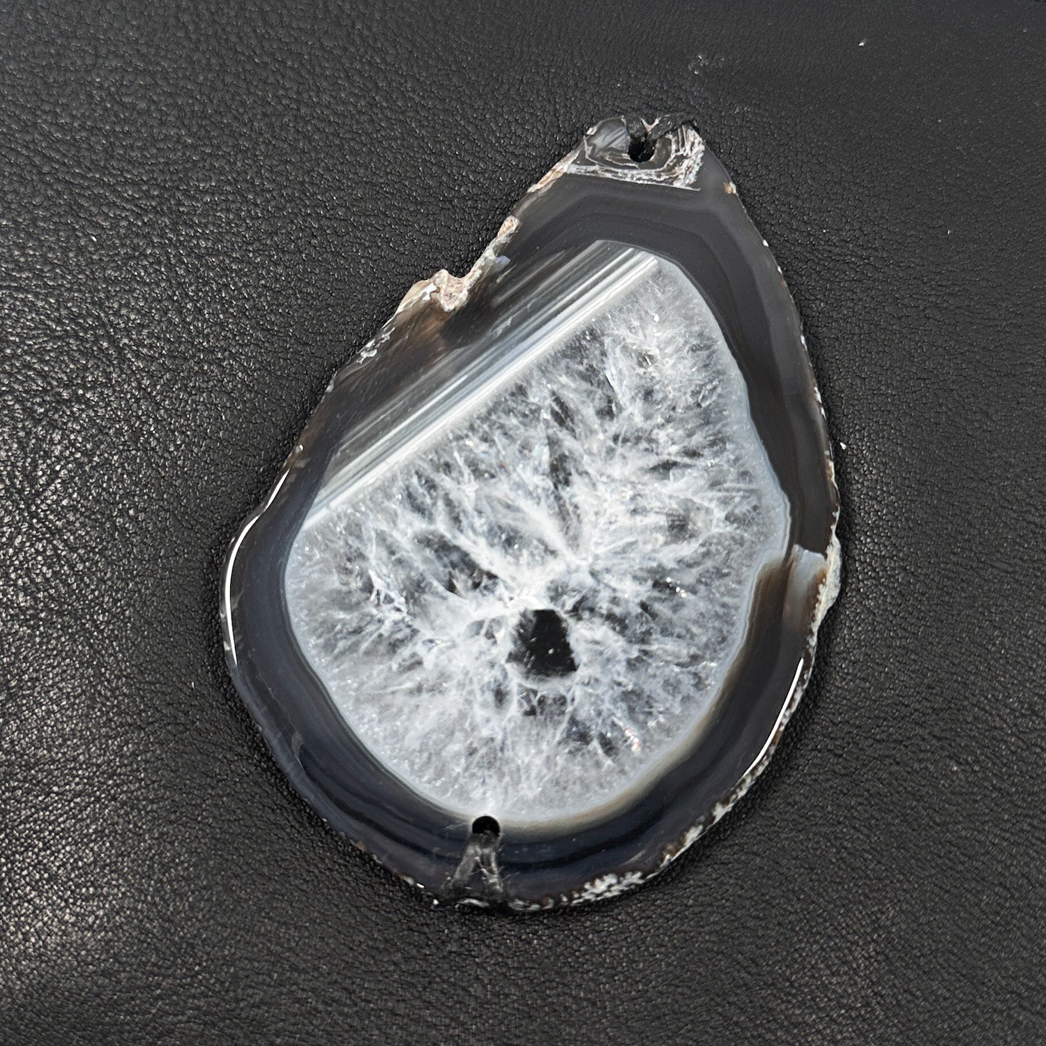 Close-up of teardrop shaped black edged agate stone with natural crystal formation on pebbled black leather.