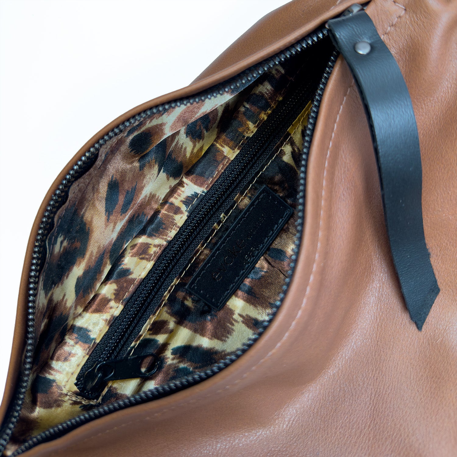 Discover the LONDON - NUTSHELL by evokewomen, a brown leather crossbody bag featuring a visible zipper and vibrant leopard print interior lining.