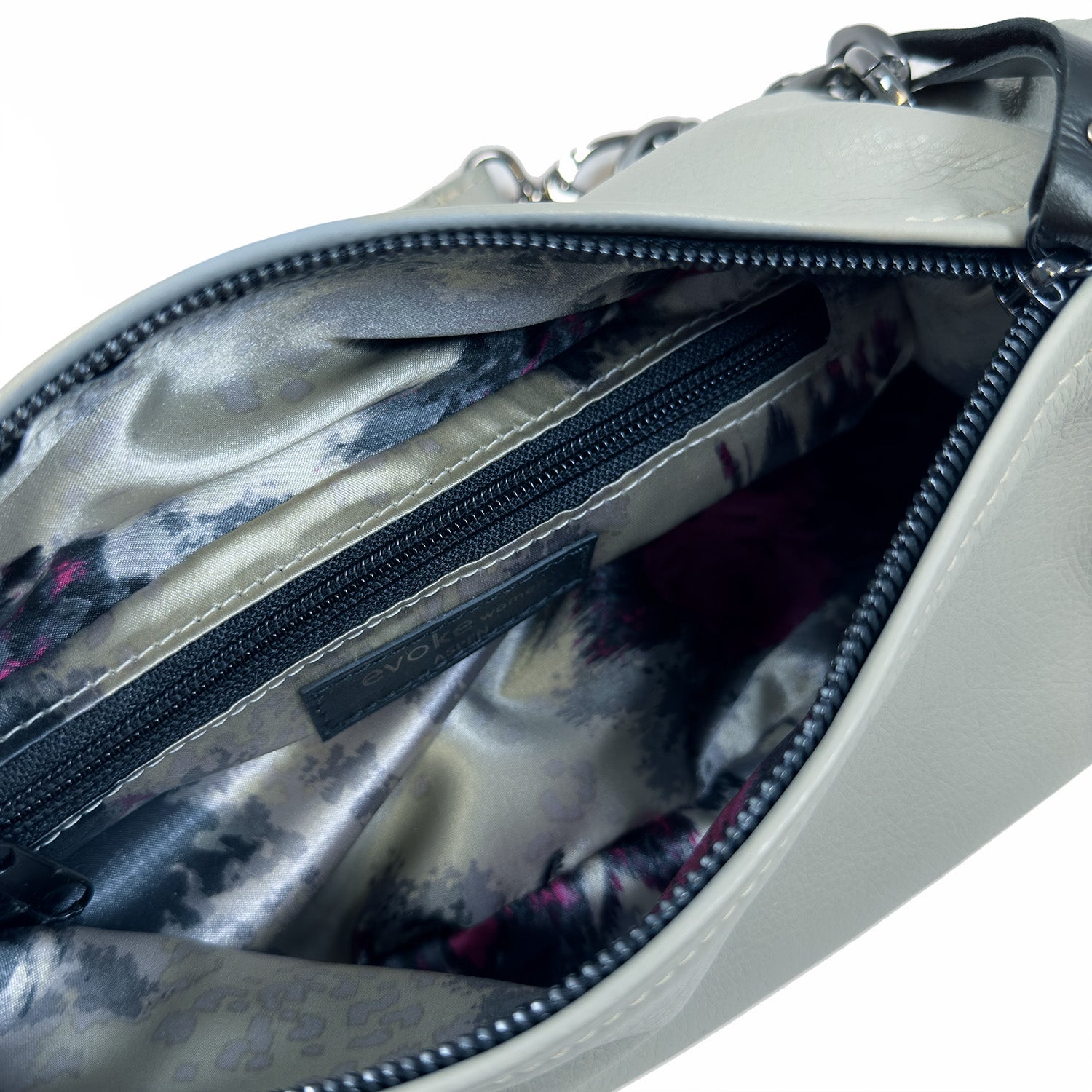 Close-up of the LONDON - LIGHT SMOKE by evokewomen, a white leather handbag with an open top that reveals a patterned interior lining and a zippered pocket, perfect for those who favor the functionality of a crossbody bag.