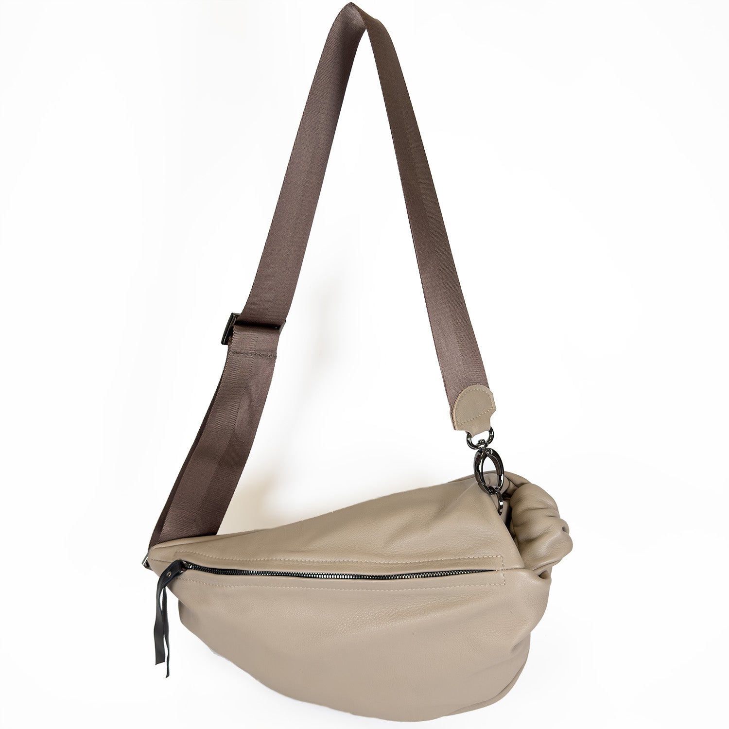 The LULA - SAND by evokewomen is a taupe leather sling bag featuring an adjustable brown strap and a zippered main compartment.