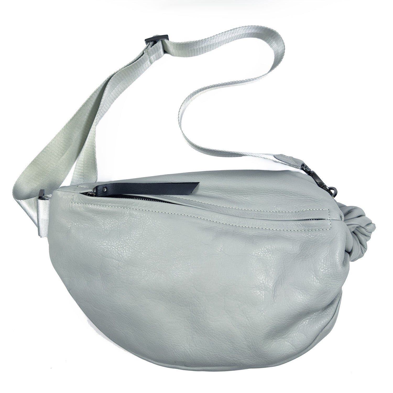 The LULA - LIGHT SMOKE sling bag by evokewomen features a light gray leather exterior, a curved shape, a wide adjustable strap, and a zippered main compartment.