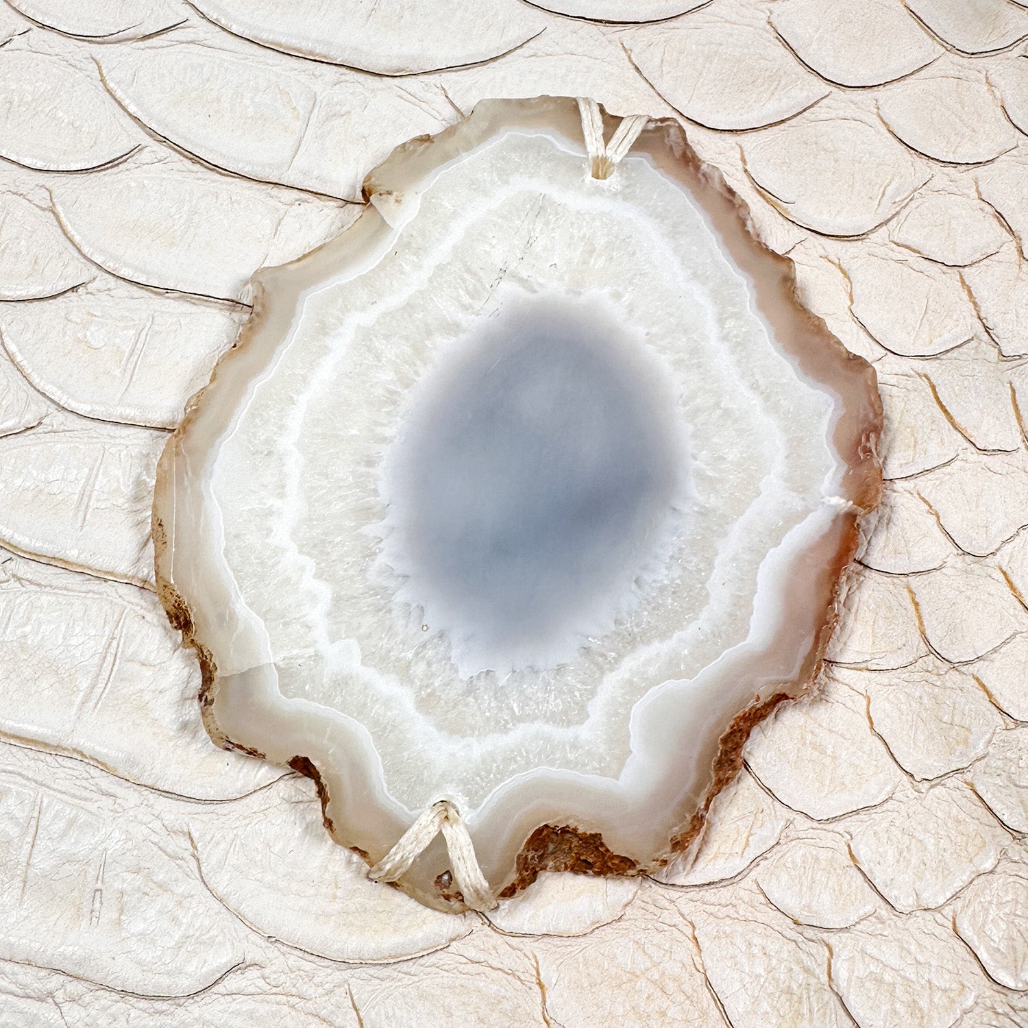 Oval shaped agate slice in variations of white and grey mounted on off white snake embossed leather.