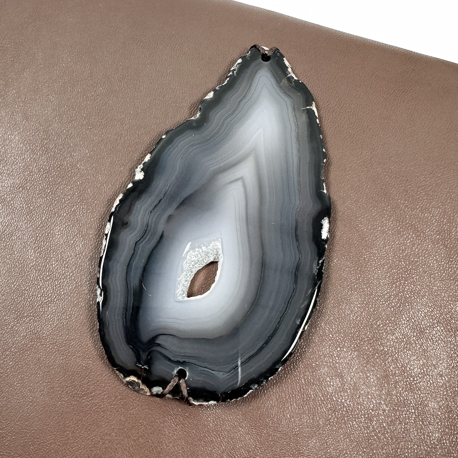 Teardrop- shaped agate slice in variations of grey mounted on brown leather.