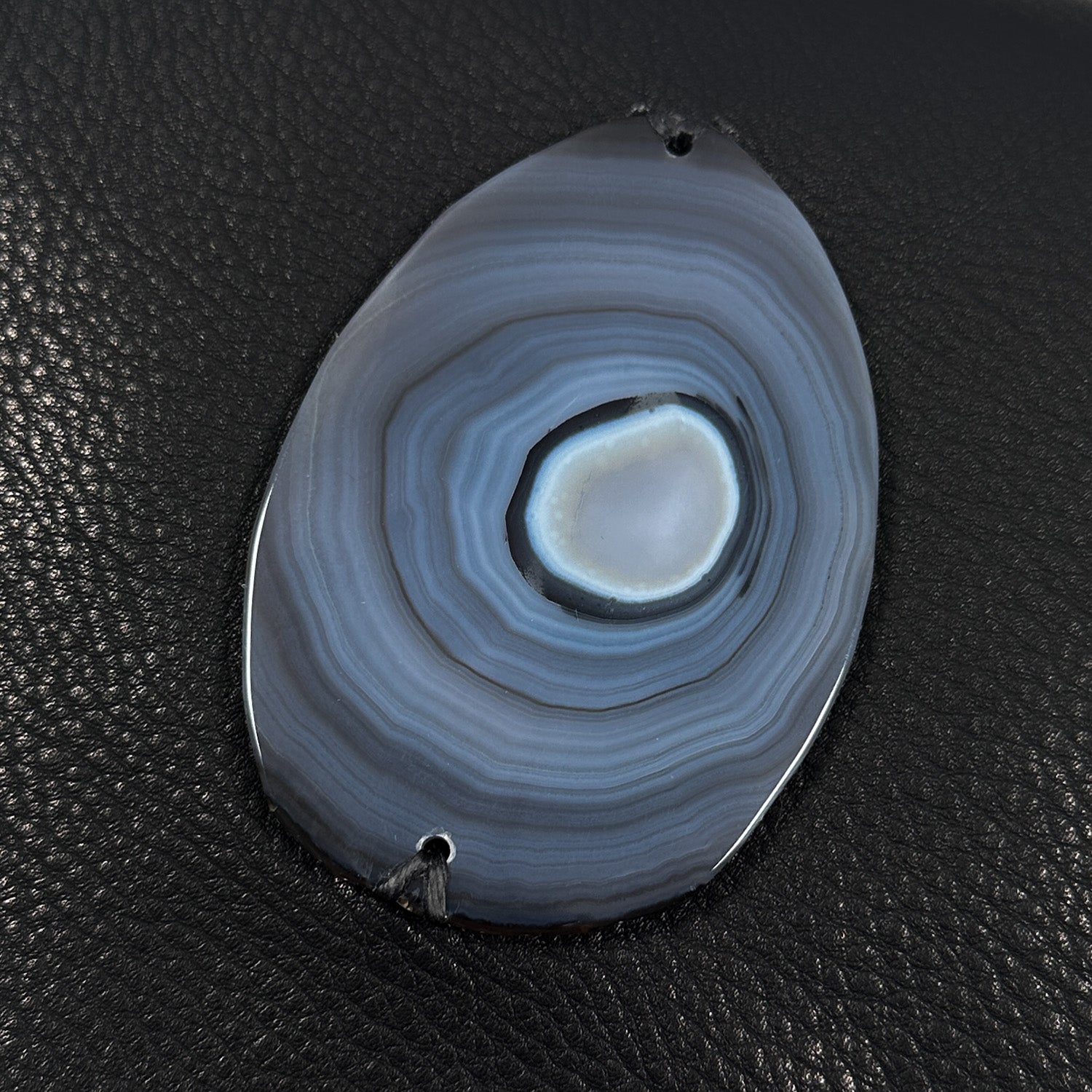 Oval shaped agate slice in variations of grey mounted on black leather.