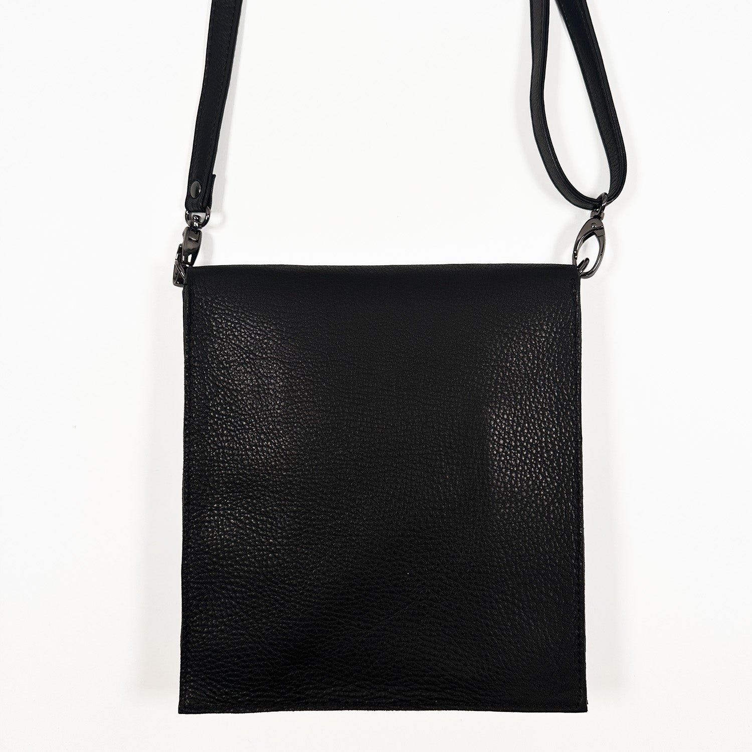 Back view of a black, portrait-shaped crossbody leather bag featuring a black leather strap and gunmetal buckles, displayed on a white background.