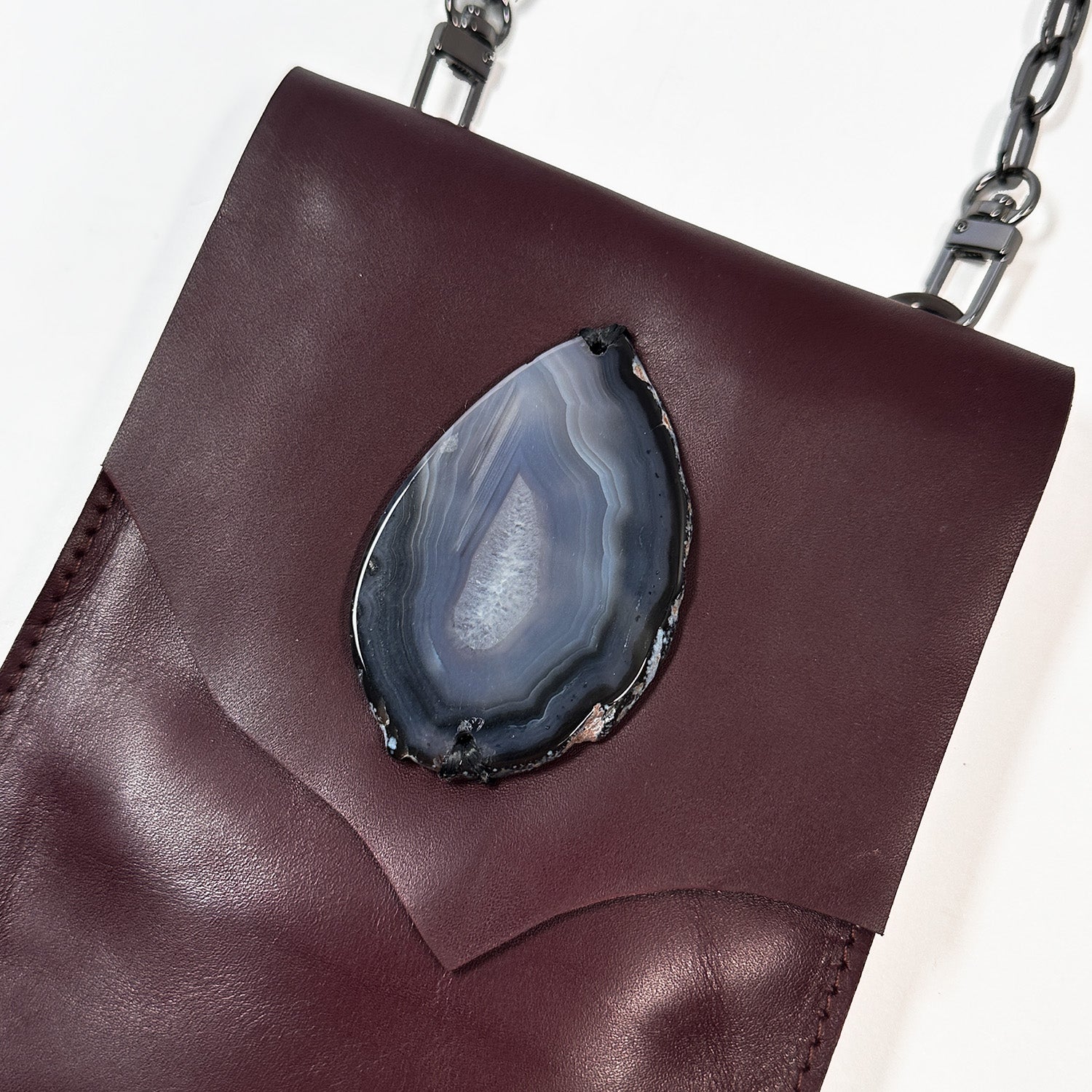 Introducing the PAULINA - burgundy by evokewomen, a crossbody bag in dark brown crafted from premium Italian leather. It features a chic chain strap and a striking teardrop-shaped agate stone on the front flap—an absolute festival essential.