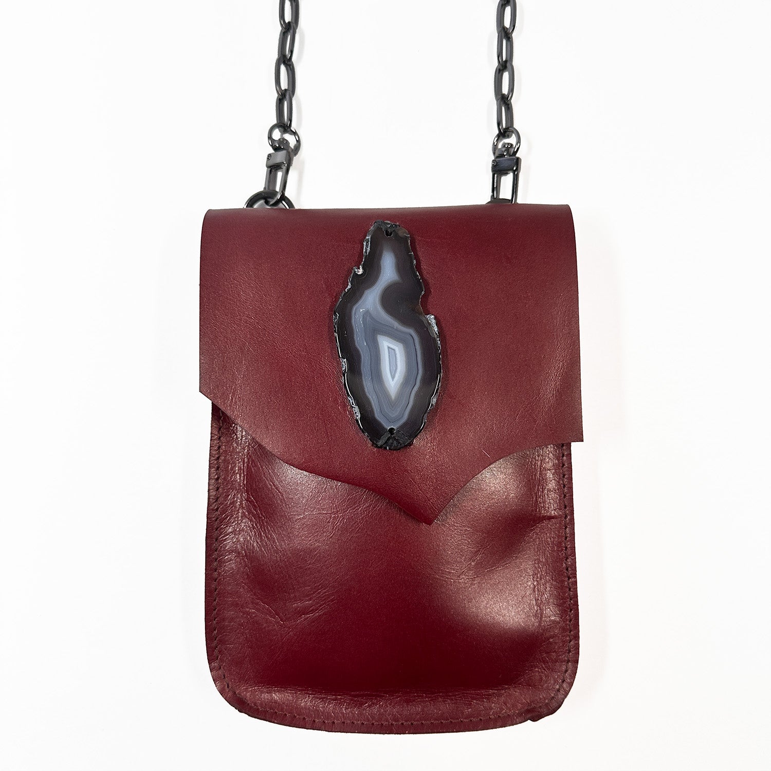 The PAULINA - wine crossbody bag by evokewomen is a compact, rectangular accessory made from Italian leather. It includes a shoulder chain and features a decorative stone on the front flap, making it a must-have for festivals.