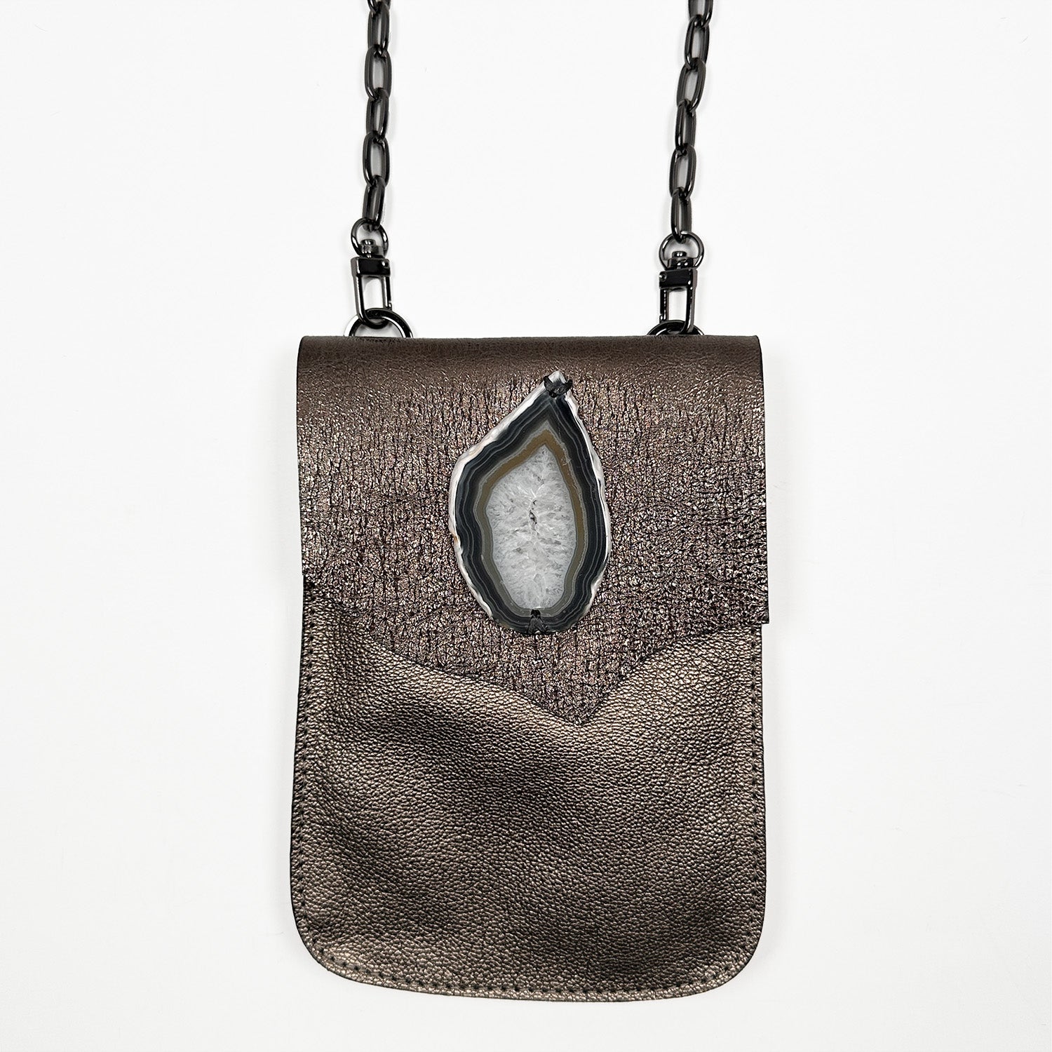 The PAULINA - BRONZE crossbody bag by evokewomen is a compact, rectangular accessory made from Italian leather. It includes a shoulder chain and features a decorative stone on the front flap, making it a must-have for festivals.