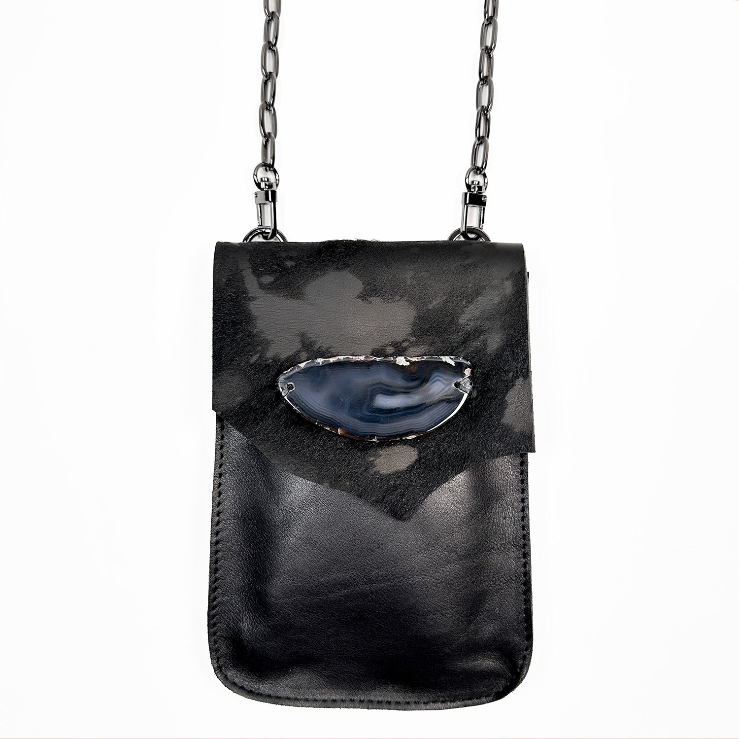 The PAULINA - BLACK FUR FLAP crossbody bag by evokewomen is a compact, rectangular accessory made from Italian leather. It includes a shoulder chain and features a decorative stone on the front flap, making it a must-have for festivals.