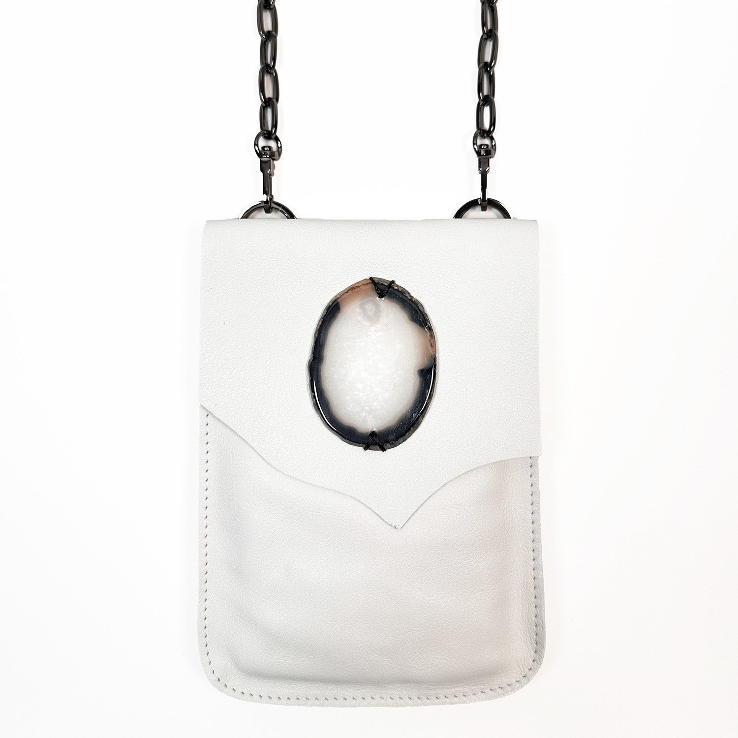 The PAULINA - white cross-body bag by evoke women boasts a chain strap and is adorned with an oval-shaped black and white stone detail on the flap.