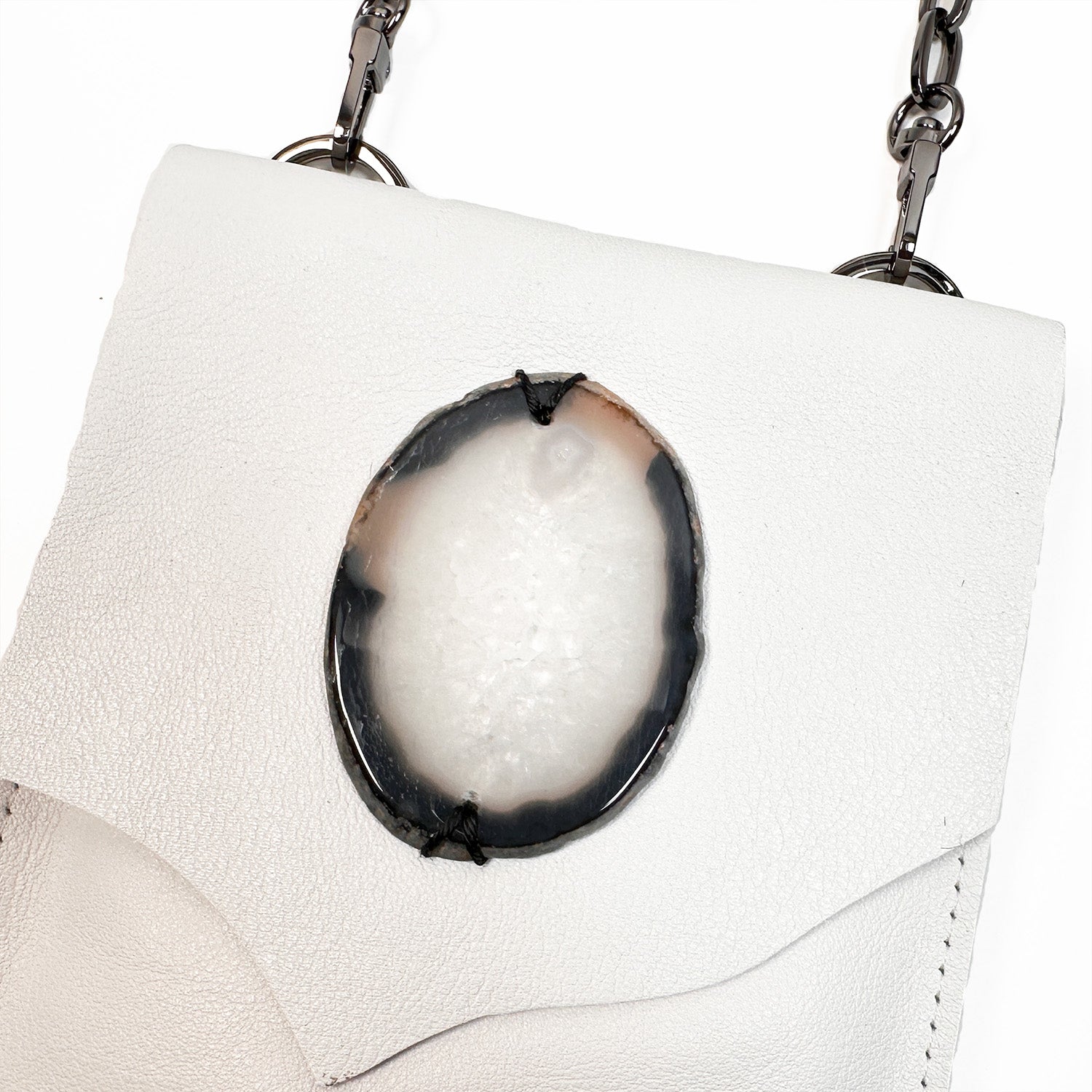The PAULINA - white by evokewomen is a chic leather crossbody bag that showcases an oval-shaped agate accent and a fashionable chain strap.
