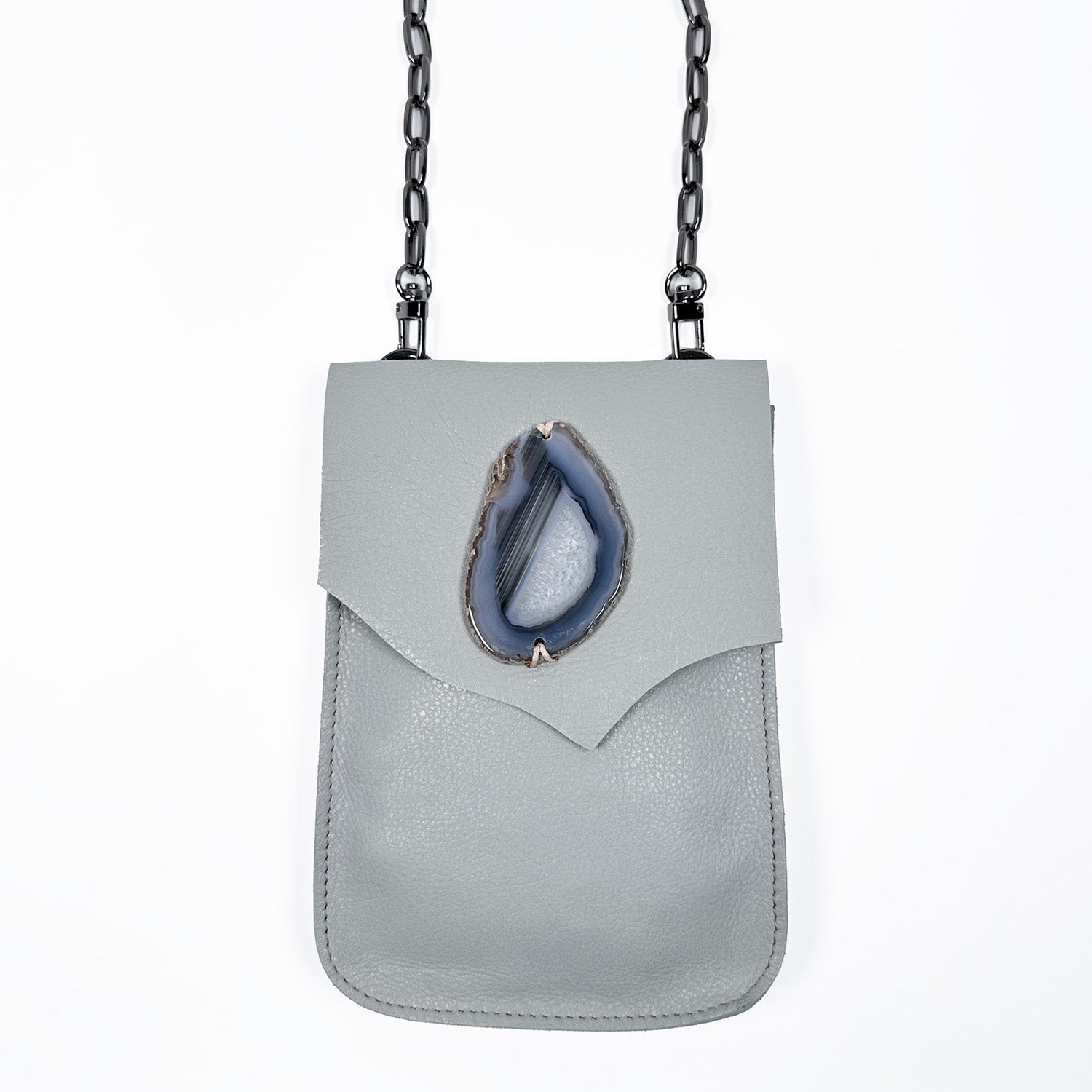 Sleek crossbody bag made from smooth smoke gray leather, featuring a pointed flap with a teardrop-shaped blue agate stone centerpiece and a bold black gunmetal chain strap.
