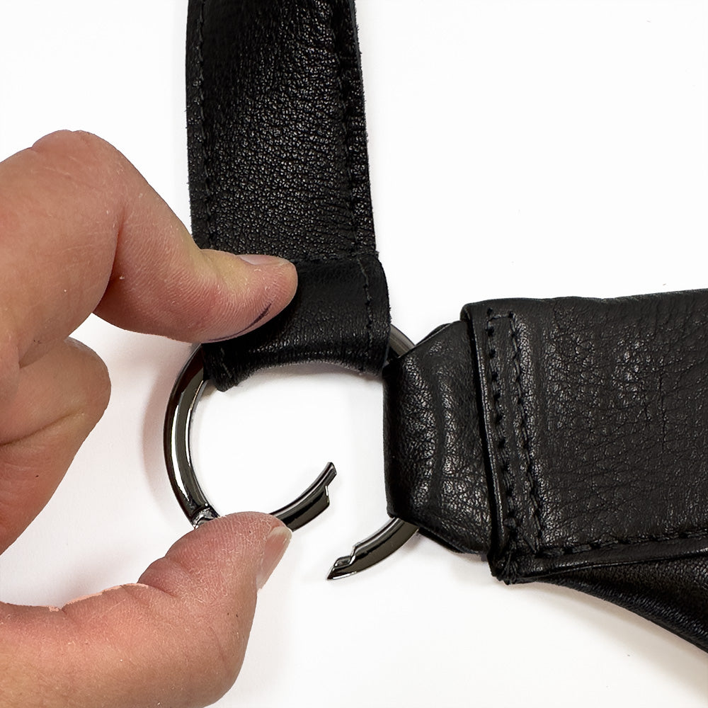 A hand holding a key ring attached to evokewomen's Sienna - black leather strap, seamlessly pairing with the stylish sling bag, its other side already connected to the ring.