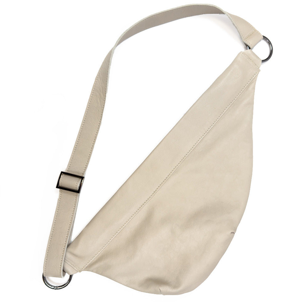 The Sienna - putty from evokewomen is a beige leather crossbody bag featuring a wide strap and metal ring accents on both ends, ideal for those who appreciate versatile style.