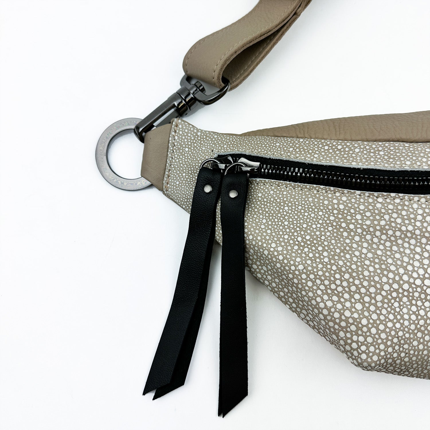 Close-up of the STELLA - SAND STINGRAY cross body bag by evokewomen, showcasing its textured beige leather design. The bag features a black zipper with two black leather pull tabs and includes a metallic ring attachment on the strap.