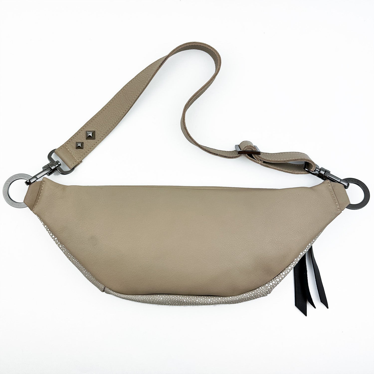 The STELLA - SAND STINGRAY by evokewomen is a tan leather sling bag featuring a curved shape, adjustable strap, and metal ring attachments.