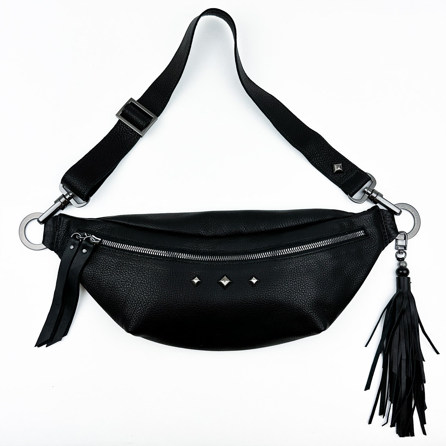 Introducing the STELLA - BLACK by evokewomen: A chic black leather bag with a zipper closure, accented with three studs and a tassel detail—ideal for versatile styling as either a crossbody or sling bag.