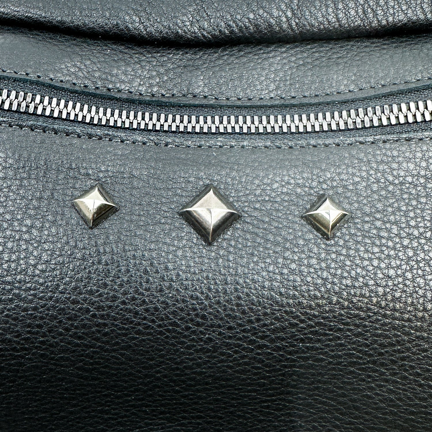 Close-up of the STELLA - BLACK sling bag by evokewomen, showcasing its black leather finish, silver zipper, and a row of three metal studs.