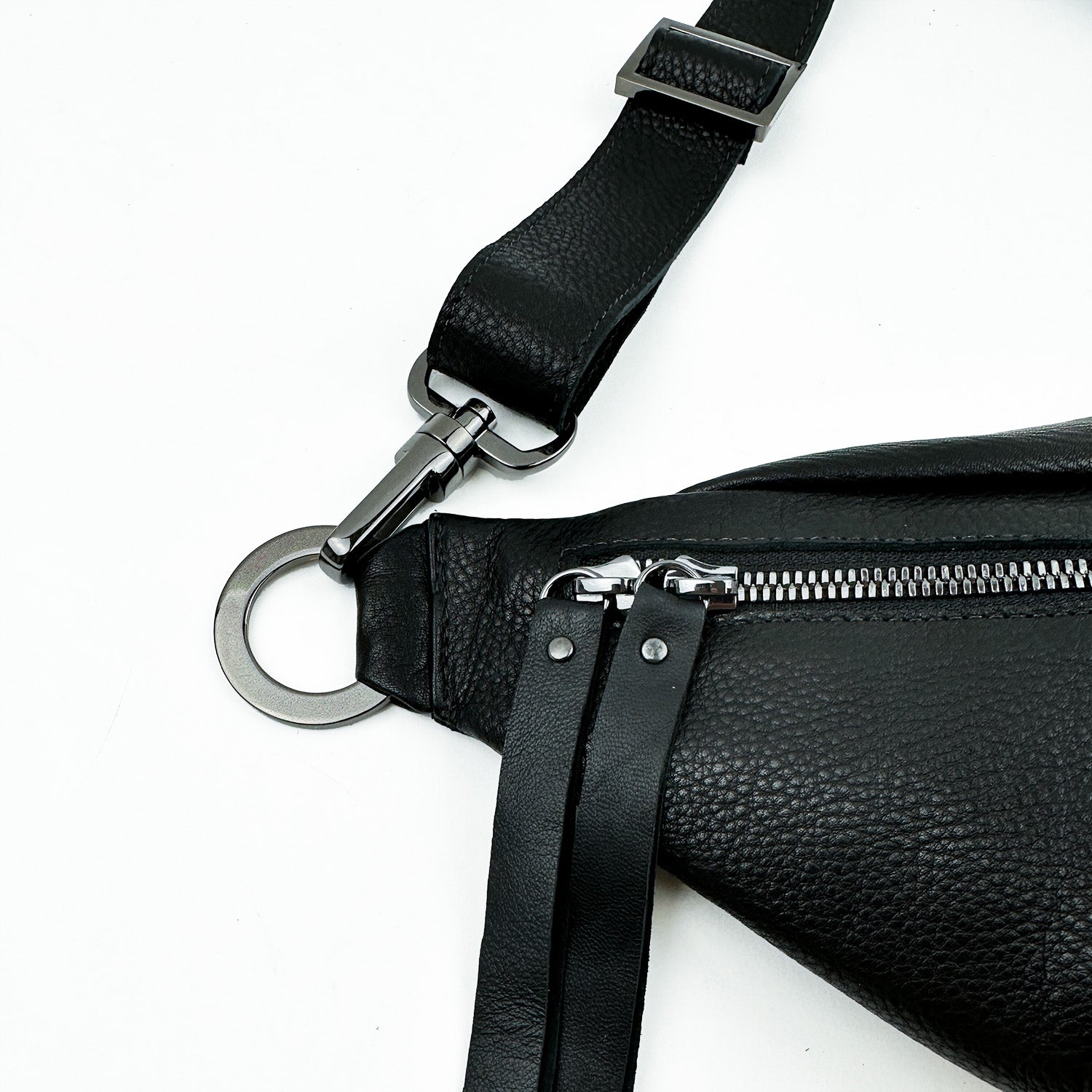 Close-up of the STELLA - BLACK, a sleek evokewomen black leather sling bag with a silver zipper, featuring metal hardware and a ring on its adjustable strap.