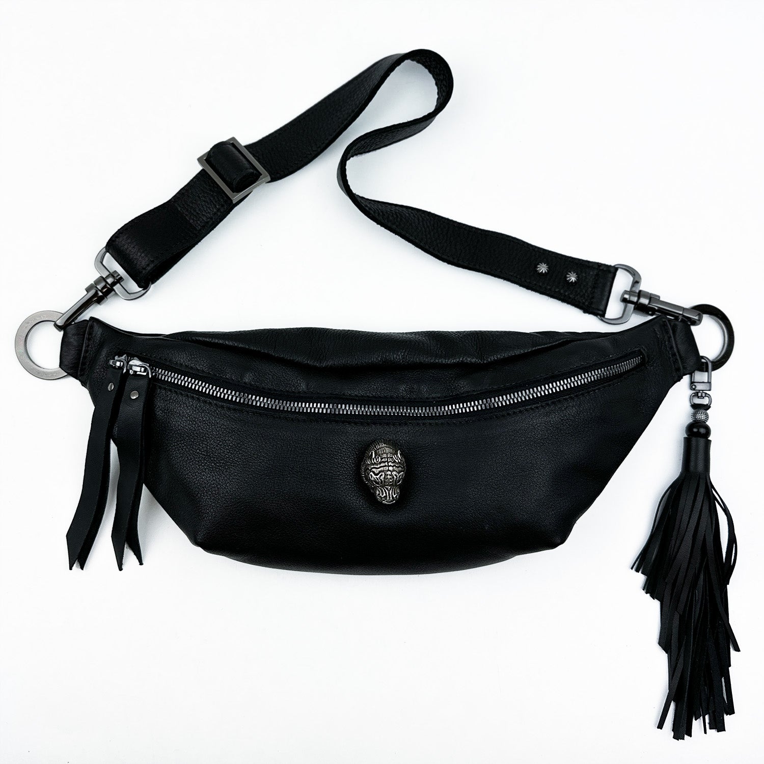 The STELLA - BLACK bag by evokewomen is a black leather belt bag that features a central zipper, decorative emblem, adjustable strap for a perfect fit, and a fringe tassel on the side.