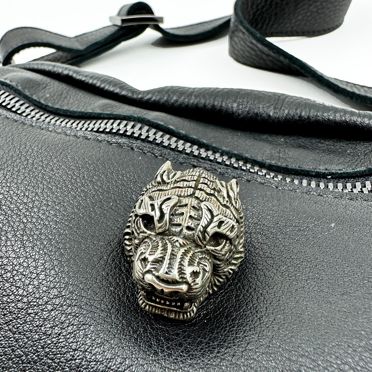 Close-up of the textured leather STELLA - BLACK bag by evokewomen, featuring a detailed metallic animal head pin and an elegant adjustable strap.