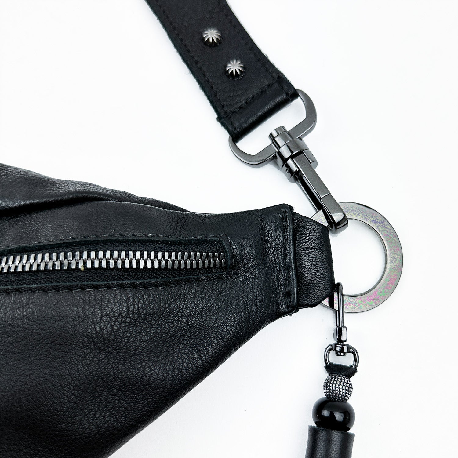 A detailed view of the STELLA - BLACK sling bag by evokewomen highlights its elegant black leather design, complemented by a metal zipper and buckle. The adjustable strap features decorative beaded accents, enhancing its stylish appeal.