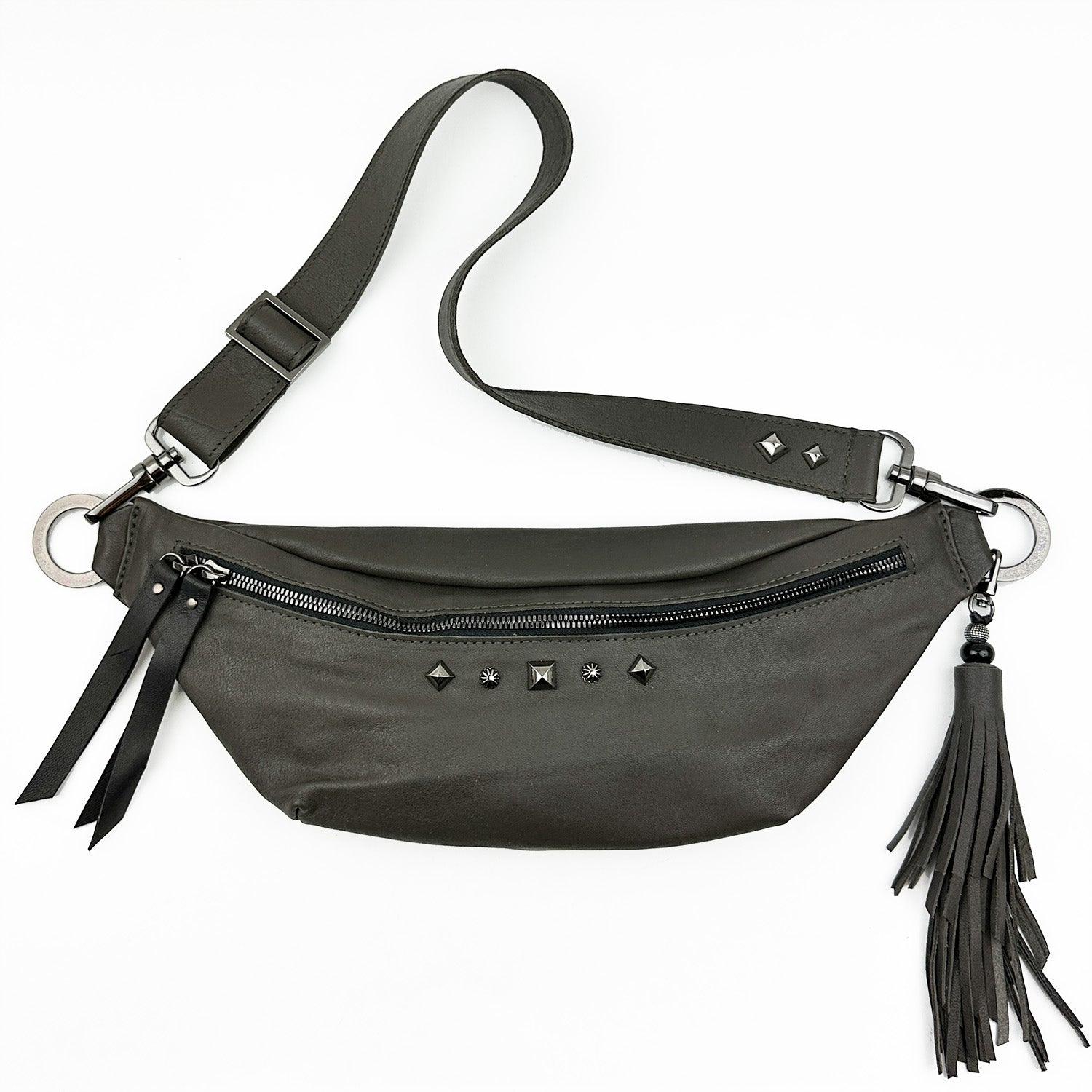 STELLA - OLIVE-GREY by evokewomen is a black leather sling bag featuring metal studs, an adjustable strap, a zipper closure, and a fringe tassel decoration.